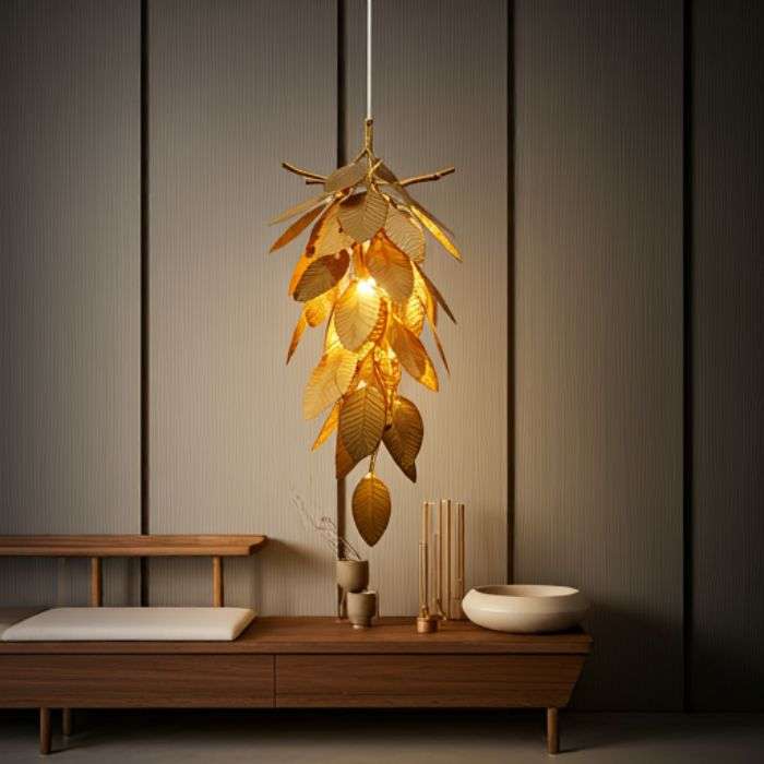 Cluster Pendant Lights: Adding Drama with Multiple Fixtures A gold-colored pendant light shaped like a cluster of leaves, hanging from a ceiling against a dark wall. The light casts a warm, inviting glow.